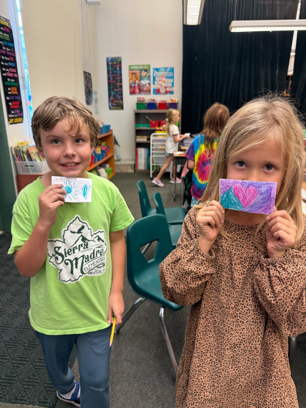 Two students holding up drawings they made at a Heart in Hand workshop